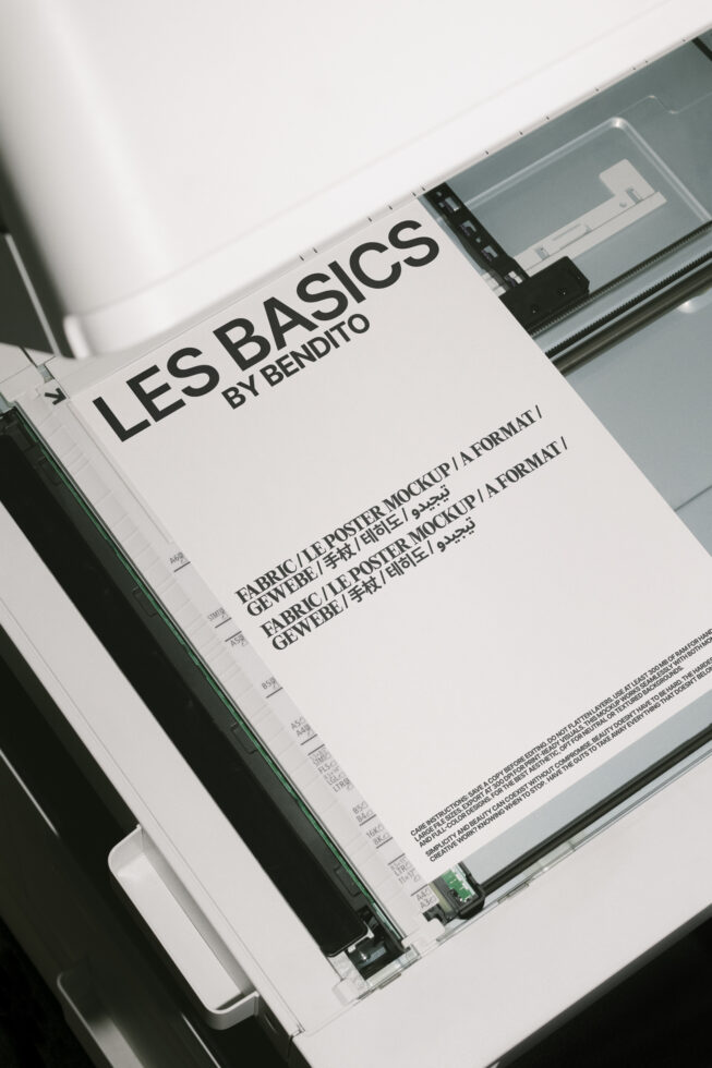 Printer scanning a mockup poster. Black text on white paper labeled Les Basics by Bendito. Perfect for designers. Keywords: Mockup, Poster, Design.