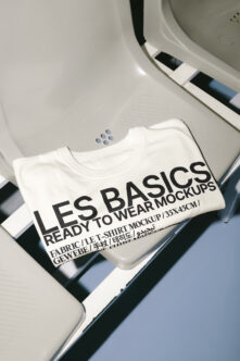 White folded t-shirt mockup with black text on neutral background with color swatches