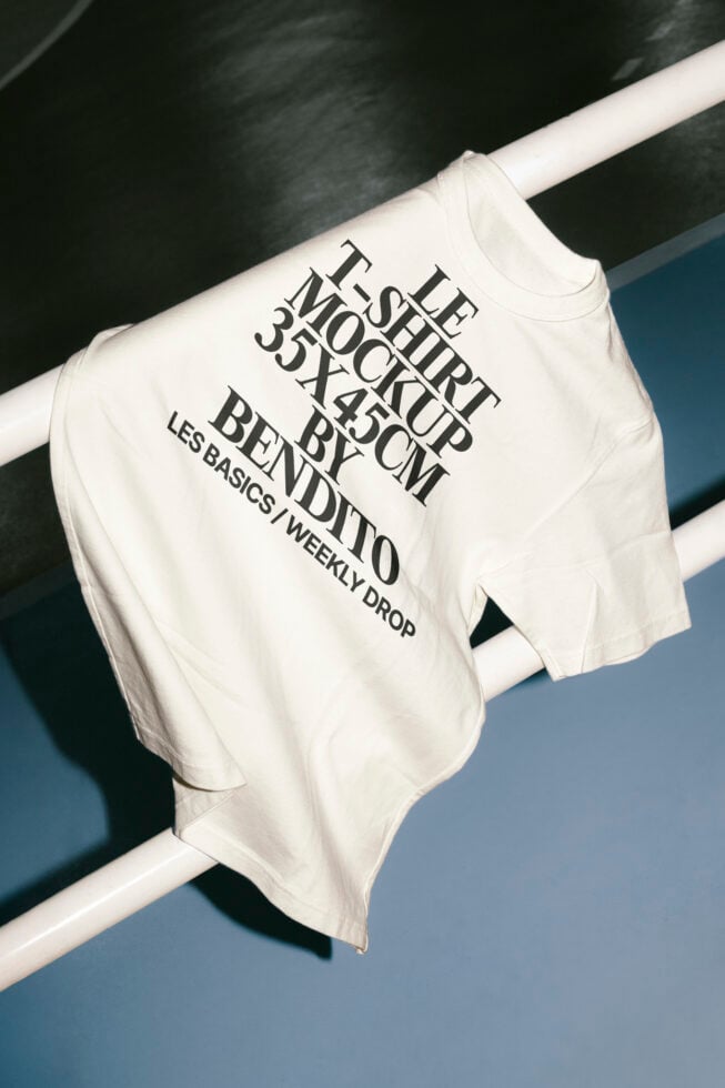 White t-shirt mockup displayed on a railing with large typography text. Ideal for fashion designers and brand presentations. High-quality graphic asset.