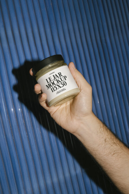 Hand holding white glass jar with black label on blue ridged background