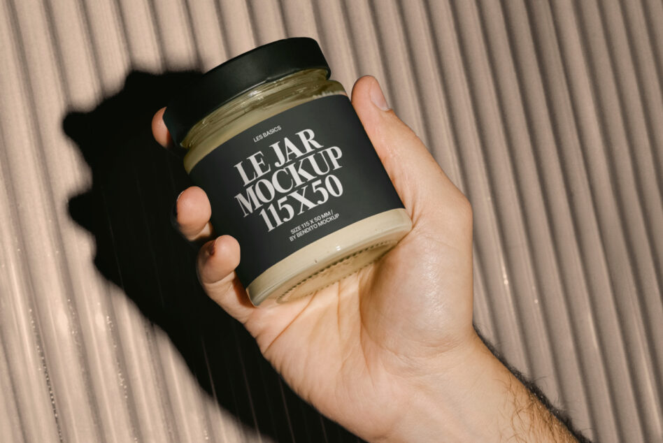 Black glass jar with cream label held in hand, striped beige background