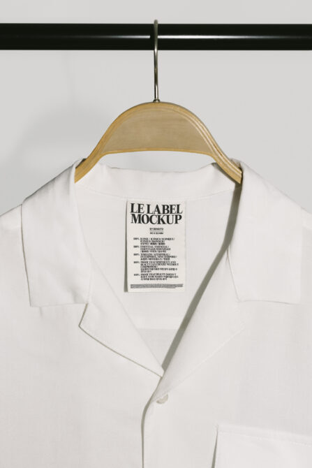Off-white collared shirt hanging from wood hanger showing black rectangular label