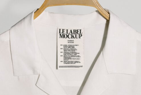 White shirt on wooden hanger displaying a detailed label mockup with multilingual text. Ideal for fashion branding presentations and design projects.