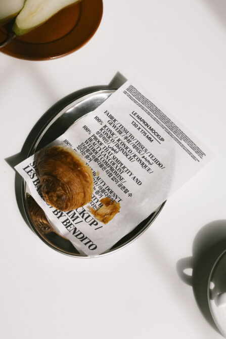 Napkin mockup featuring text on paper under a pastry on a metal tray. Ideal for showcasing designs. Keywords: mockup, design, template, graphics.