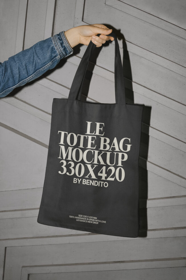 Hand holding a black tote bag mockup 330x420 mm with bold white text perfect for designers looking for high-quality branding and packaging templates.