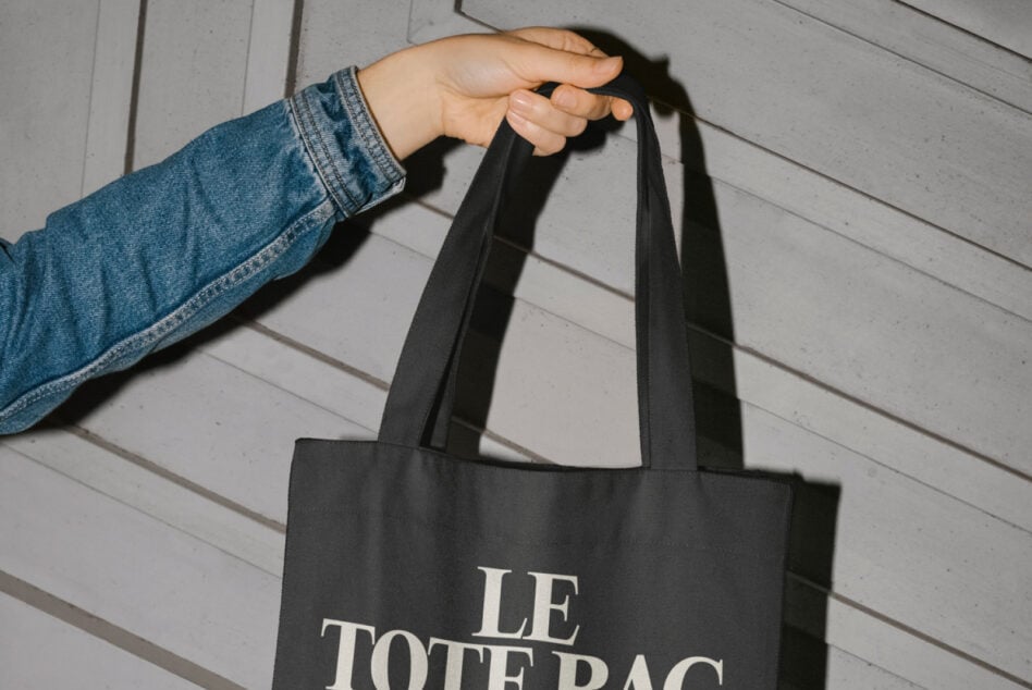 Close up of black tote bag handles with Le Tote Bag text visible on fabric surface