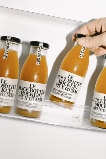 Hand holding juice bottle with white label among similar bottles on white surface