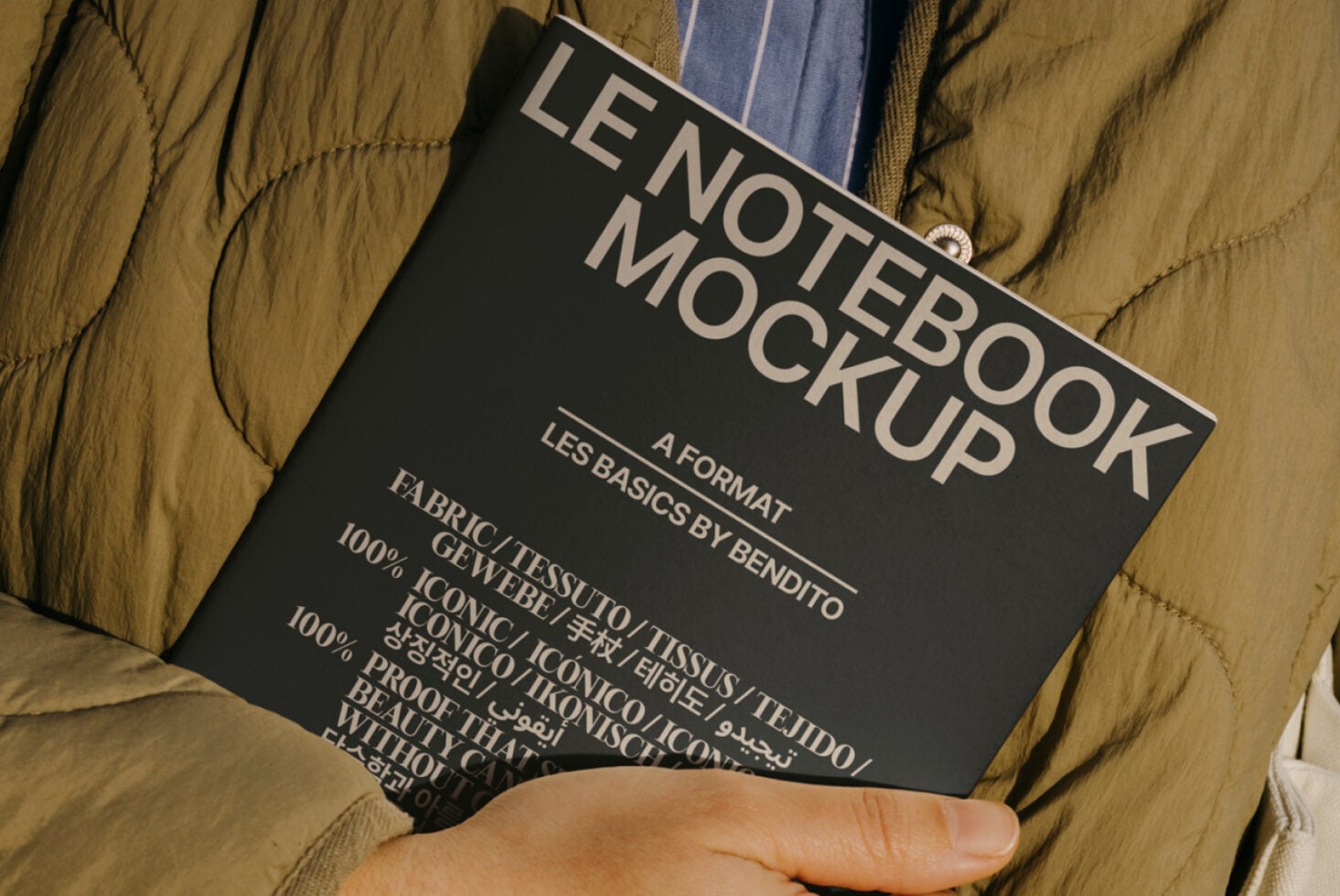 Dark notebook label mock-up on quilted olive jacket with man's hand
