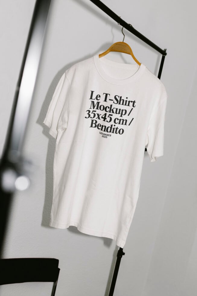 White T-shirt mockup hanging on a wooden hanger with simple black text design. Perfect for designers creating apparel templates and graphics.