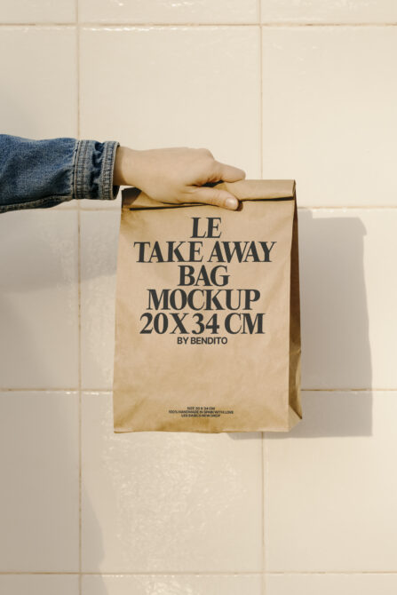 Child's hand holding kraft paper takeaway bag with Le Takeaway Bag Mockup text by Bendito