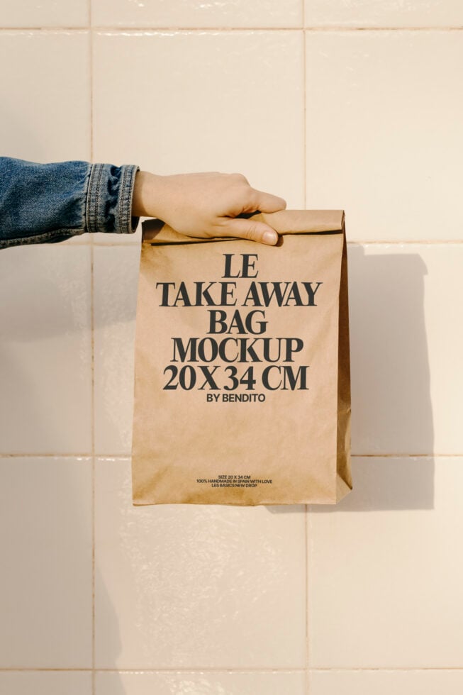 Hand holding a recyclable paper bag mockup against a tiled background. Ideal for showcasing packaging designs in graphic design projects.
