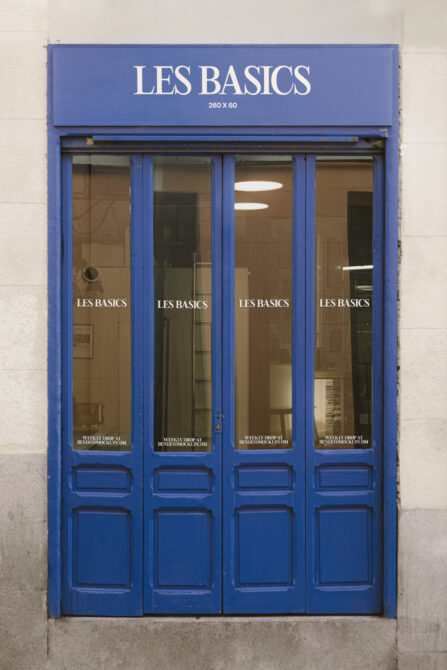 Blue storefront with white Les Basics text on glass doors with dark panels below