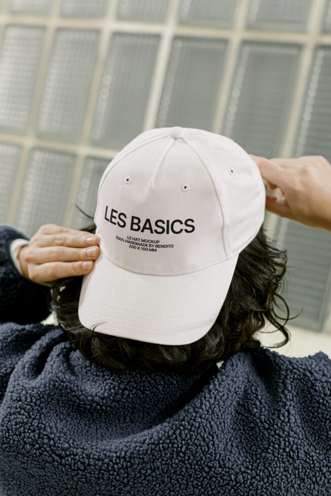 Back view of person adjusting white cap with text Les Basics. Cap design mockup template for designers. Ideal for apparel graphics and branding projects.
