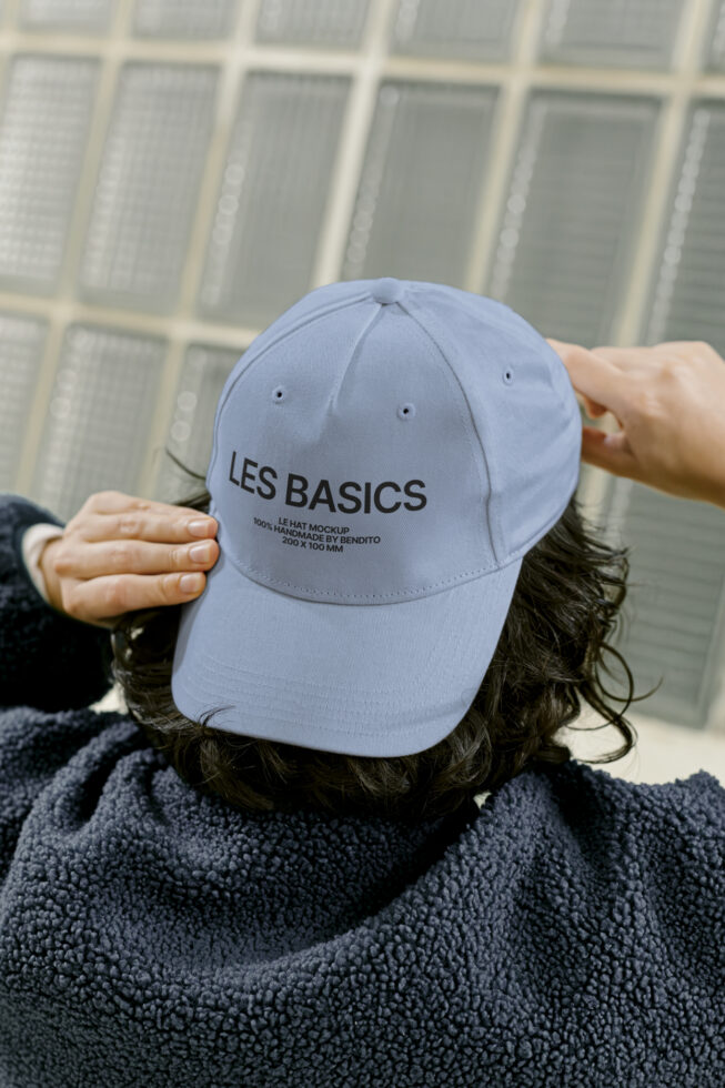 Blue cap mockup with text Les Basics on a person in a cozy fleece jacket. Ideal for designers seeking customizable hat templates for branding projects.