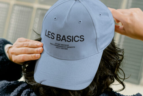Close-up of a person adjusting a light blue cap with the text LES BASICS. Perfect for showcasing hat mockup templates and apparel design graphics.