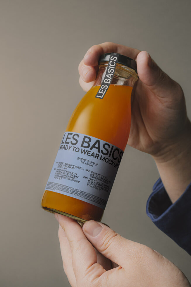 Hand holding a glass bottle with a customizable label for design mockups. Perfect for showcasing branding projects. Ideal for designers needing templates.