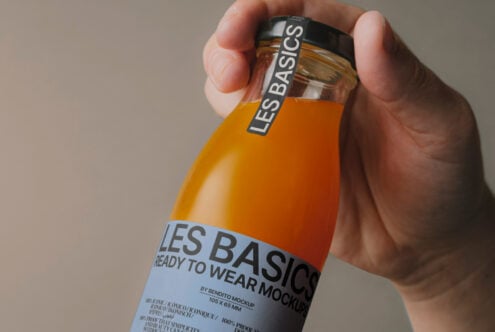 Hand holding orange juice bottle mockup with label design les basics ready to wear mockups ideal for designers and graphic projects SEO*>Mockups