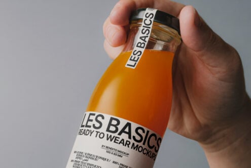Hand holding an orange juice bottle labeled Les Basics with mockup design on white background perfect for packaging presentations designers assets.