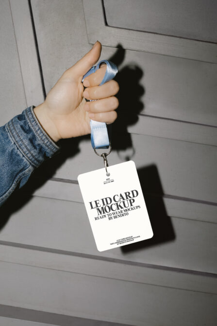 Hand holding white ID badge on blue lanyard against concrete wall