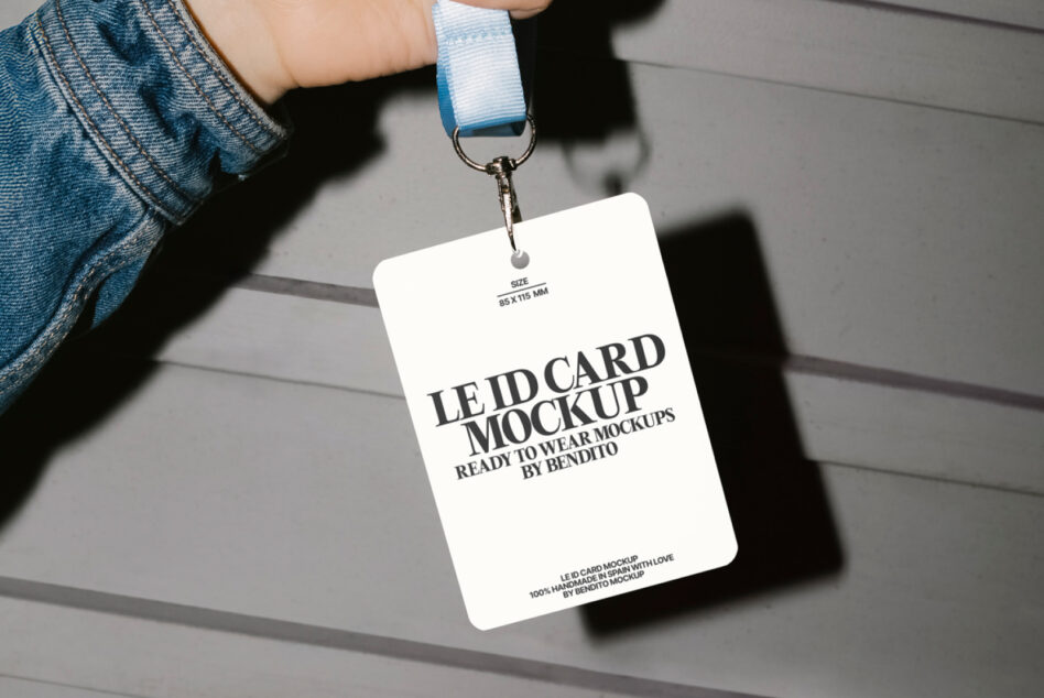 Hand holding white ID badge on light blue lanyard against concrete wall
