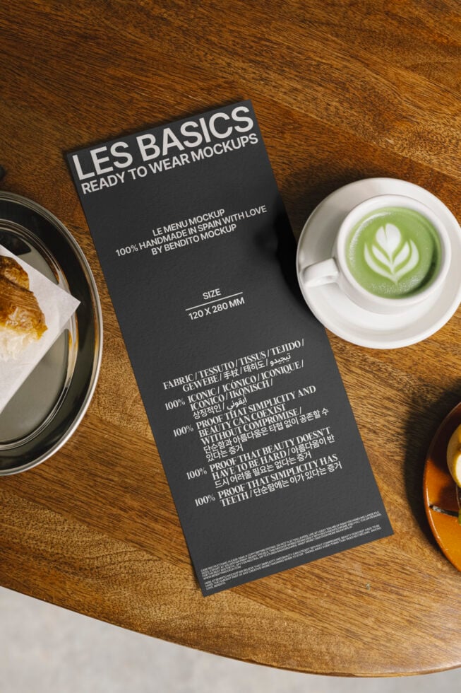 Black menu mockup on wooden table with latte art coffee and pastry. Perfect for designers seeking high-quality templates and mockups for branding.