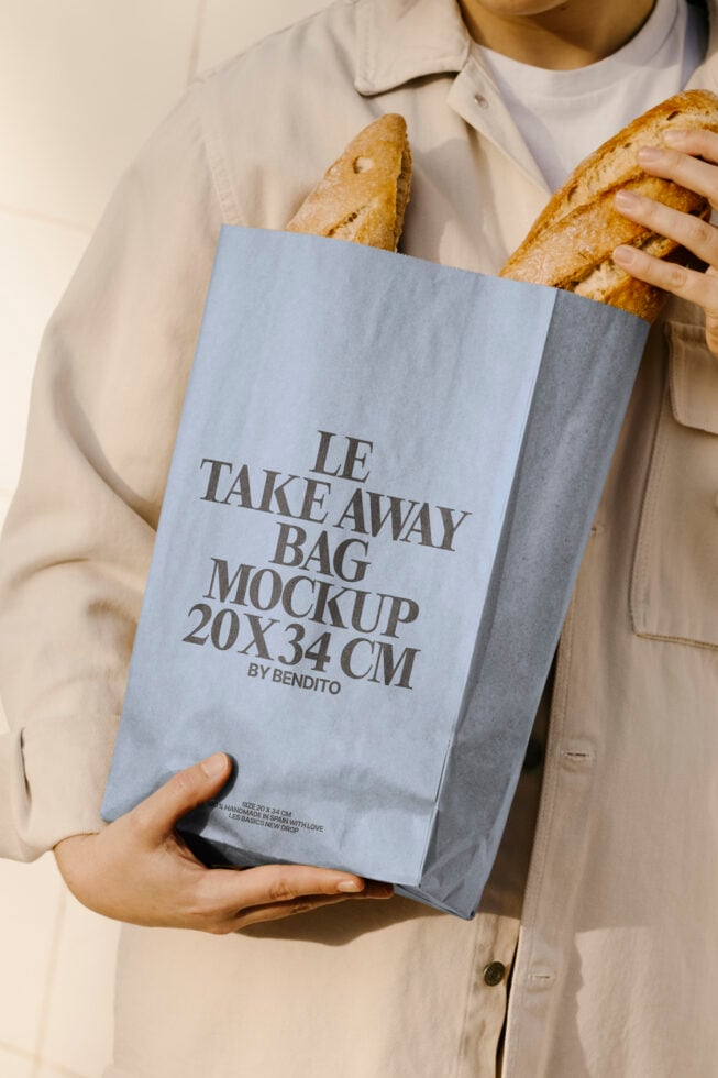 Person holding a blue paper bag with Le Take Away Bag Mockup text, ideal for bakery branding and packaging design. Perfect for designers seeking templates.