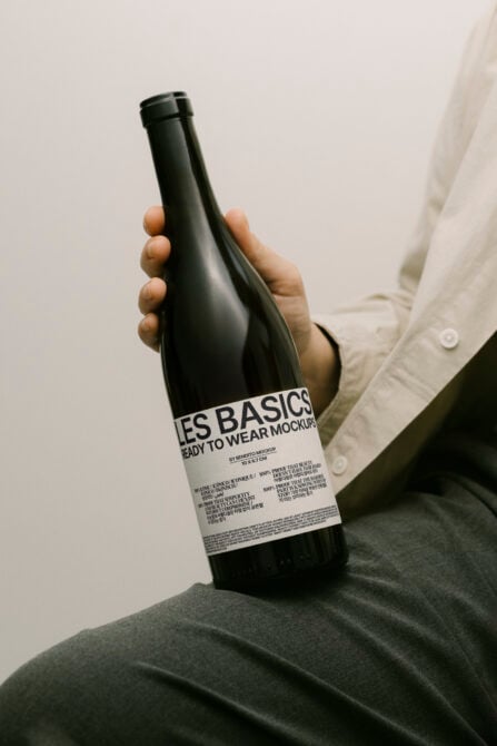 Black wine bottle with white label held in hand, cream shirt visible