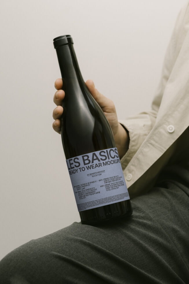 Person holding wine bottle with label mockup. Dark bottle on neutral background. Perfect for branding designers and product presentation. Mockup asset.