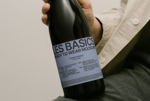 Hand holding wine bottle with minimalist label design mockup. Label reads Les Basics ready to wear mockups. Perfect for designers and branding projects.
