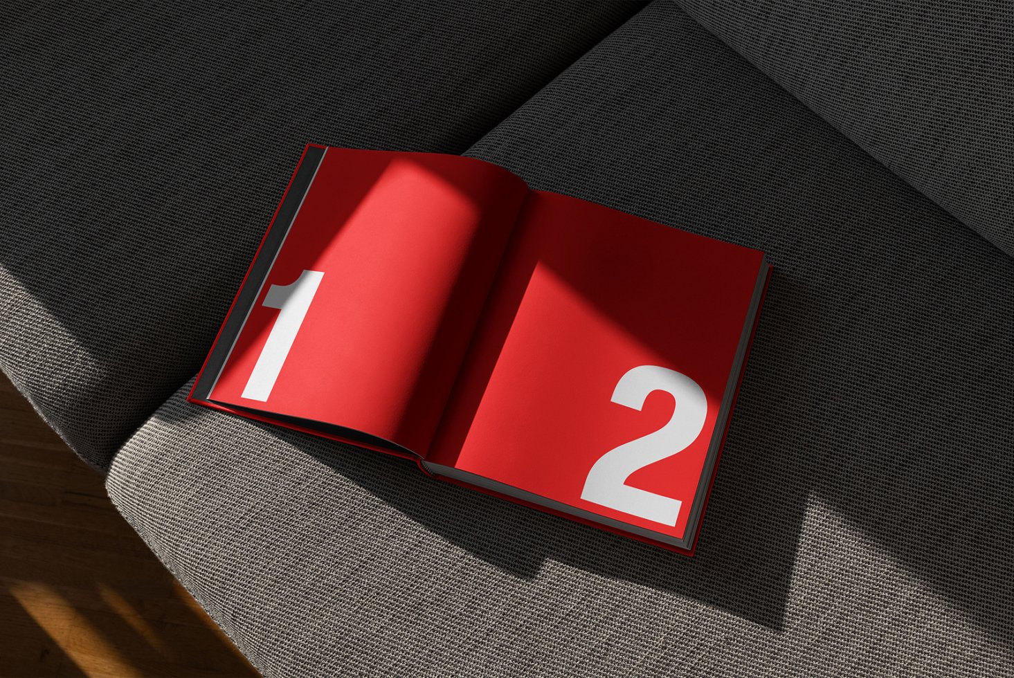 Open magazine mockup on gray sofa with bold white numbers one and two on red pages. Perfect for designers seeking modern graphic templates and layouts.
