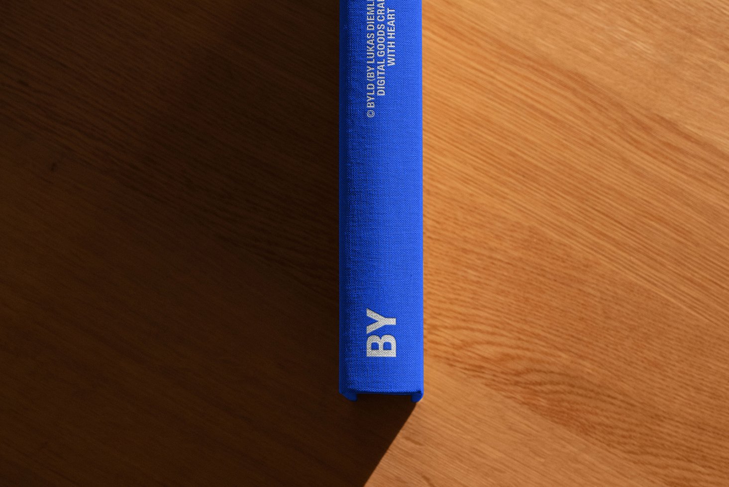 Blue hardcover book spine with white text placed on wooden surface. Ideal for graphic designers seeking high-quality book cover mockup templates.