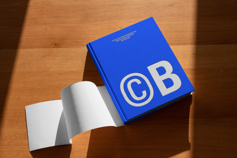 Bright blue hardcover with circular logo, open pages visible, wood table backdrop