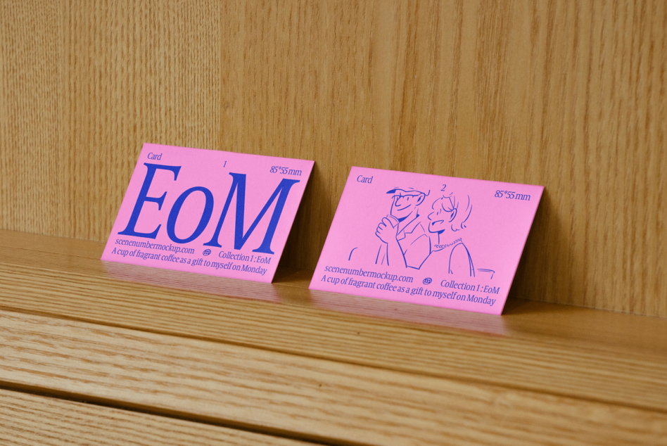 Bright pink business cards with EoM lettering propped on wooden table