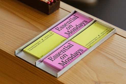 Desk setting with pink and yellow business cards reading Essential on Mondays. Perfect for mockups templates design inspiration. Creative workspace.