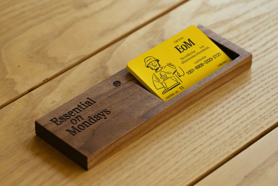 Yellow business card on dark wood block with Essential on Mondays branding