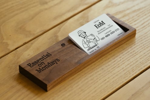 Wooden business card holder with engraved text holds white card featuring a minimalist illustration. Ideal for office desk organization or display mockup.