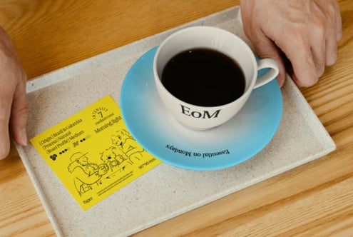 Coffee cup on blue saucer with design print on wooden tray holding a yellow coffee info card ideal for graphic template and mockup use for designers.