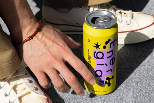 Close-up of a hand near a vibrant energy drink can, sneakers visible in the background, ideal for mockups and branding kits for designers.