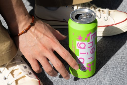 Close-up of a hand next to a bright green energy drink can and white sneakers on a gray surface. Mockups Photography Graphic Design Inspiration.