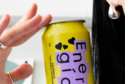 Hand holding a vibrant yellow energy drink can with modern black typography and heart icons. Ideal for branding and packaging mockups.