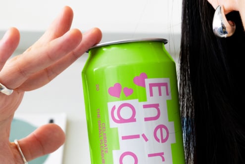 Close-up of a hand holding a vibrant green energy drink can with bold pink text and heart graphics. Perfect for beverage packaging mockups and design projects.