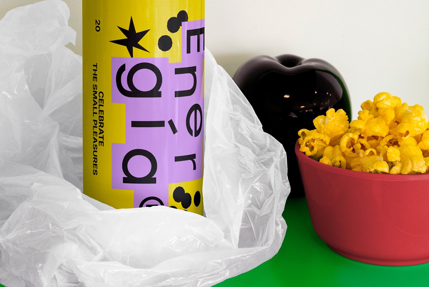 Colorful energy drink can with bold typography next to popcorn bowl and decor object. Suitable for mockup, graphic design projects, branding assets.