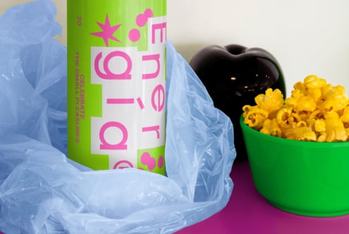 Bright energy drink can mockup on pink background with popcorn in green bowl. Blue plastic wrap adds vibrant contrast. Perfect for graphic design projects.