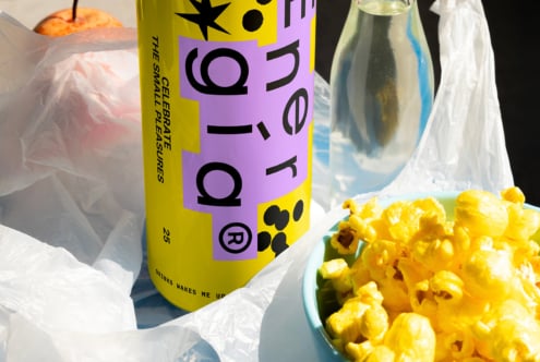 Colorful beverage can with vibrant typography, next to a glass bottle, apple, and popcorn. Ideal for graphic designers seeking fresh mockup inspiration.
