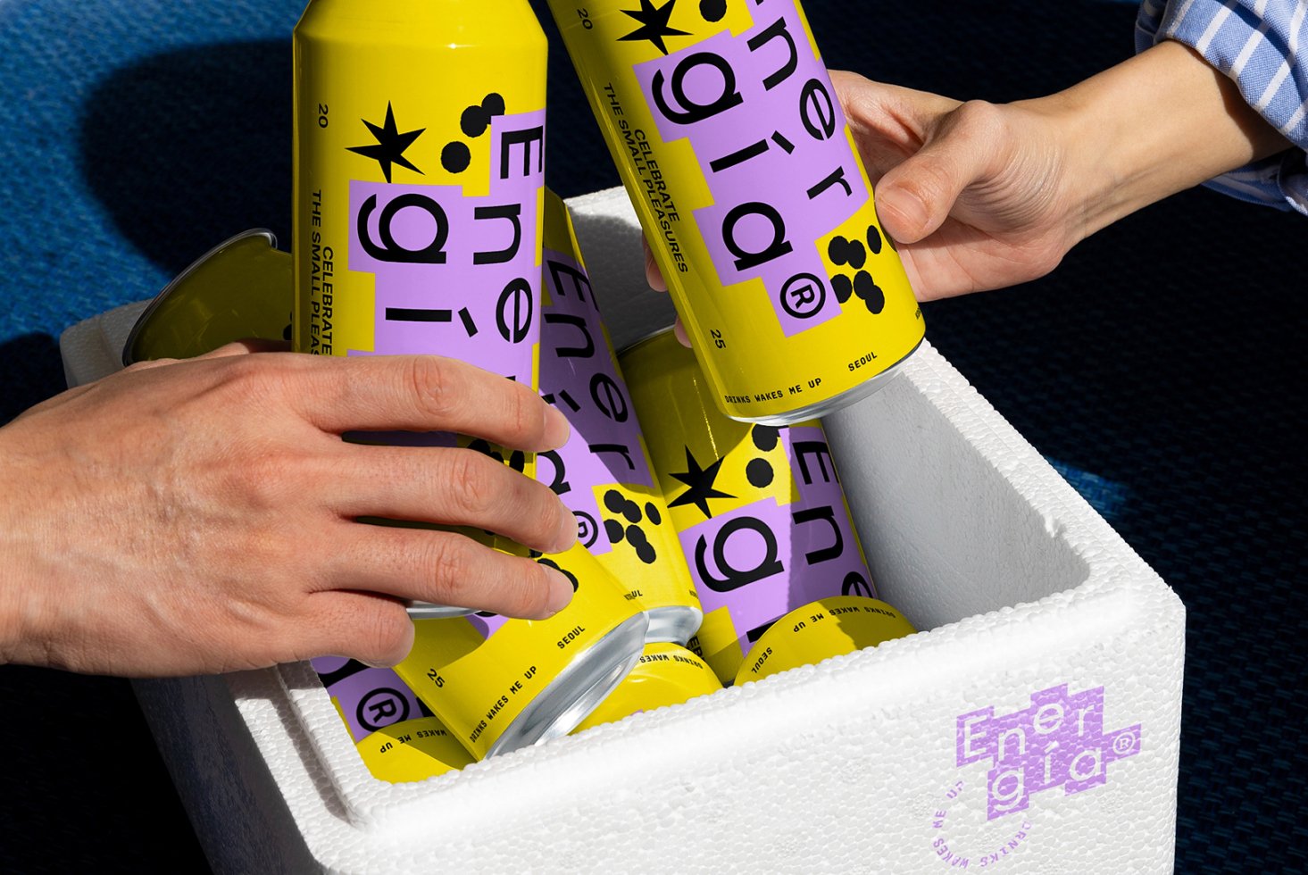 Hands reaching for vibrant energy drink cans with colorful branding in a white cooler. Perfect for graphic designers seeking unique packaging mockups.