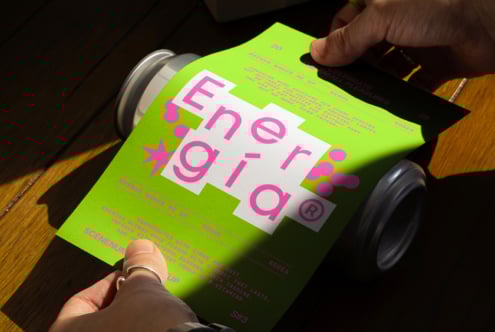 Hand holding a vibrant green and pink flyer design over a wooden table, highlighting bold typography and graphic elements suitable for print mockups.