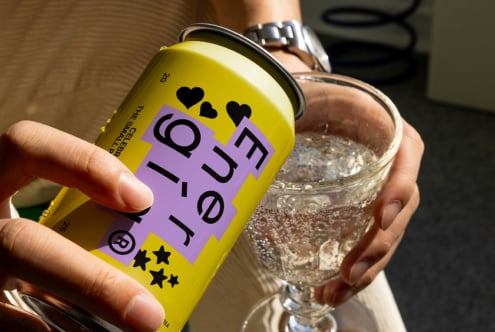 Hand pouring sparkling beverage from a yellow can with modern graphic design into a clear glass suitable for mockups or templates for designers