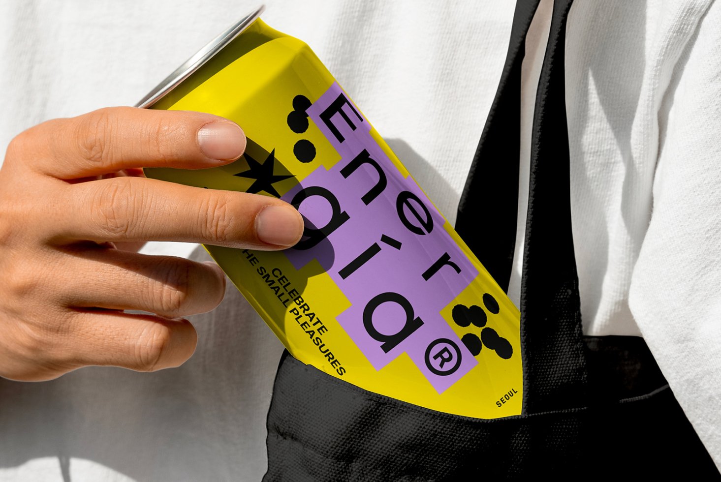 Hand holding a vibrant yellow and purple energy drink can design mockup placed in a bag ideal for branding designers and packaging projects