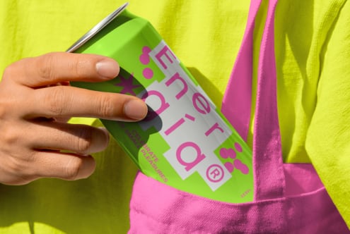Hand holding a vibrant green energy drink can with pink text against a neon yellow shirt and pink bag. Perfect for mockup designs and graphics.