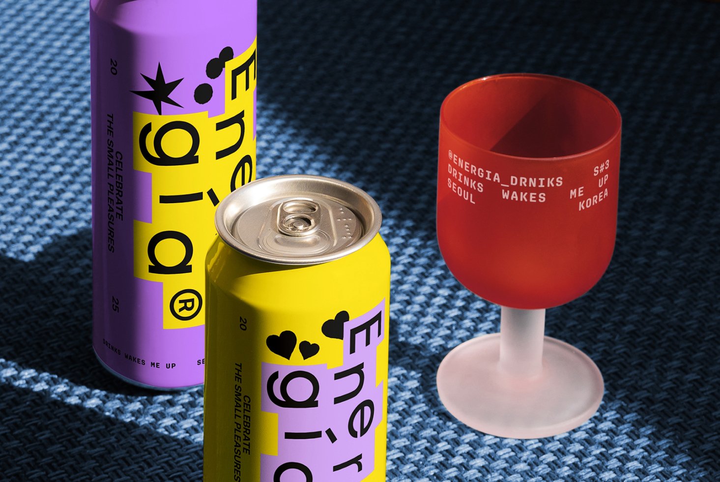 Colorful energy drink cans and a branded cup on a blue textured surface. Vibrant packaging design for beverage mockup. Ideal for graphic designers.